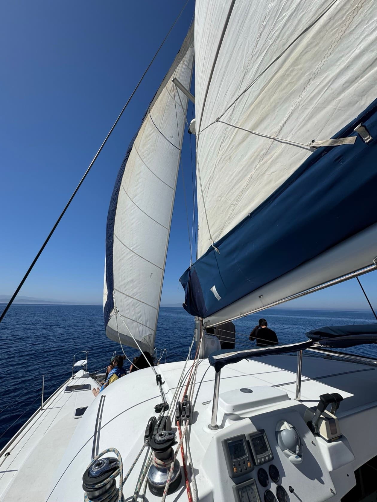 Cubierta de un catamarán navegando, con las velas y pasajeros