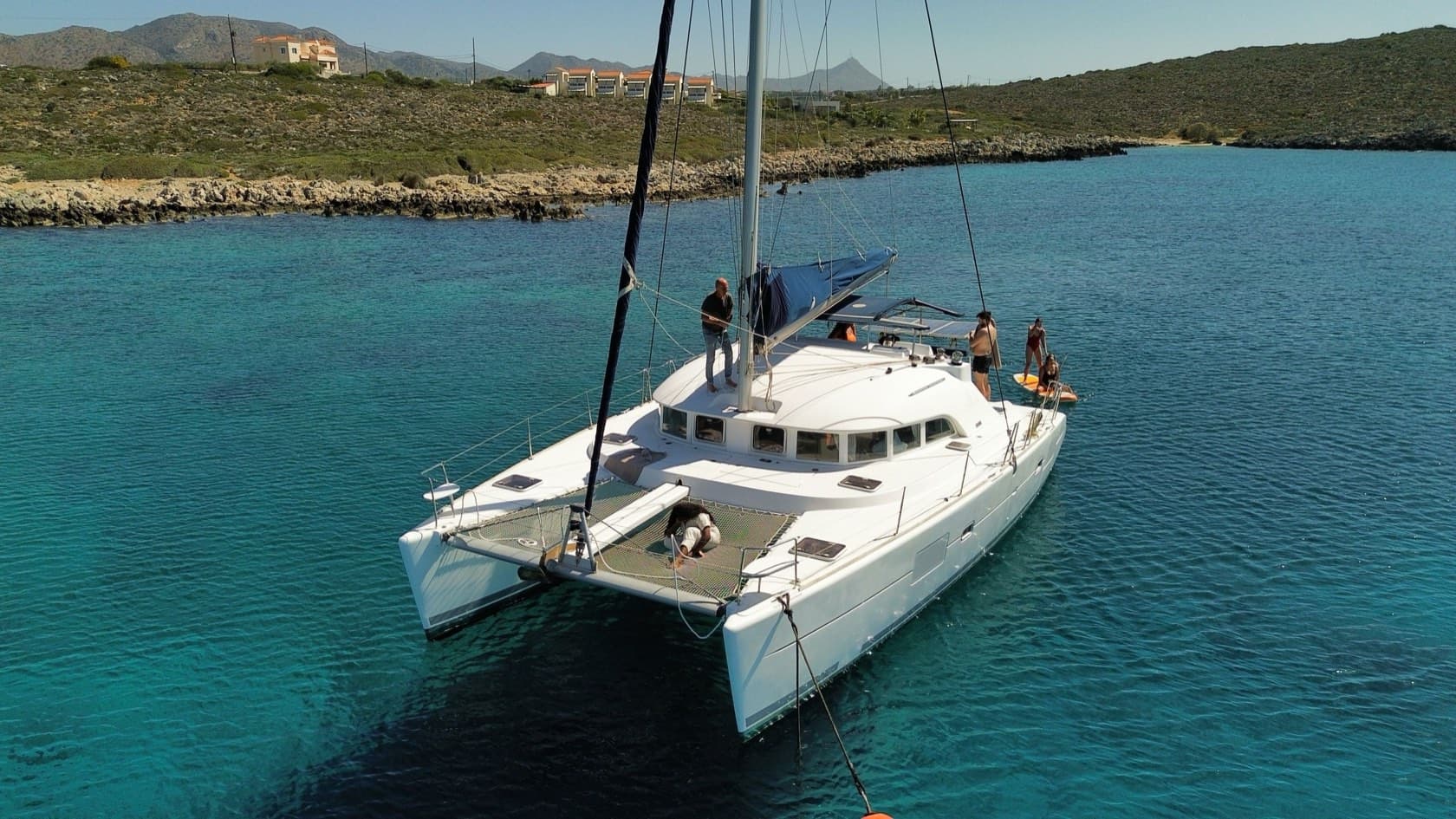 Catamarán fondeado en una caleta turquesa de costa rocosa