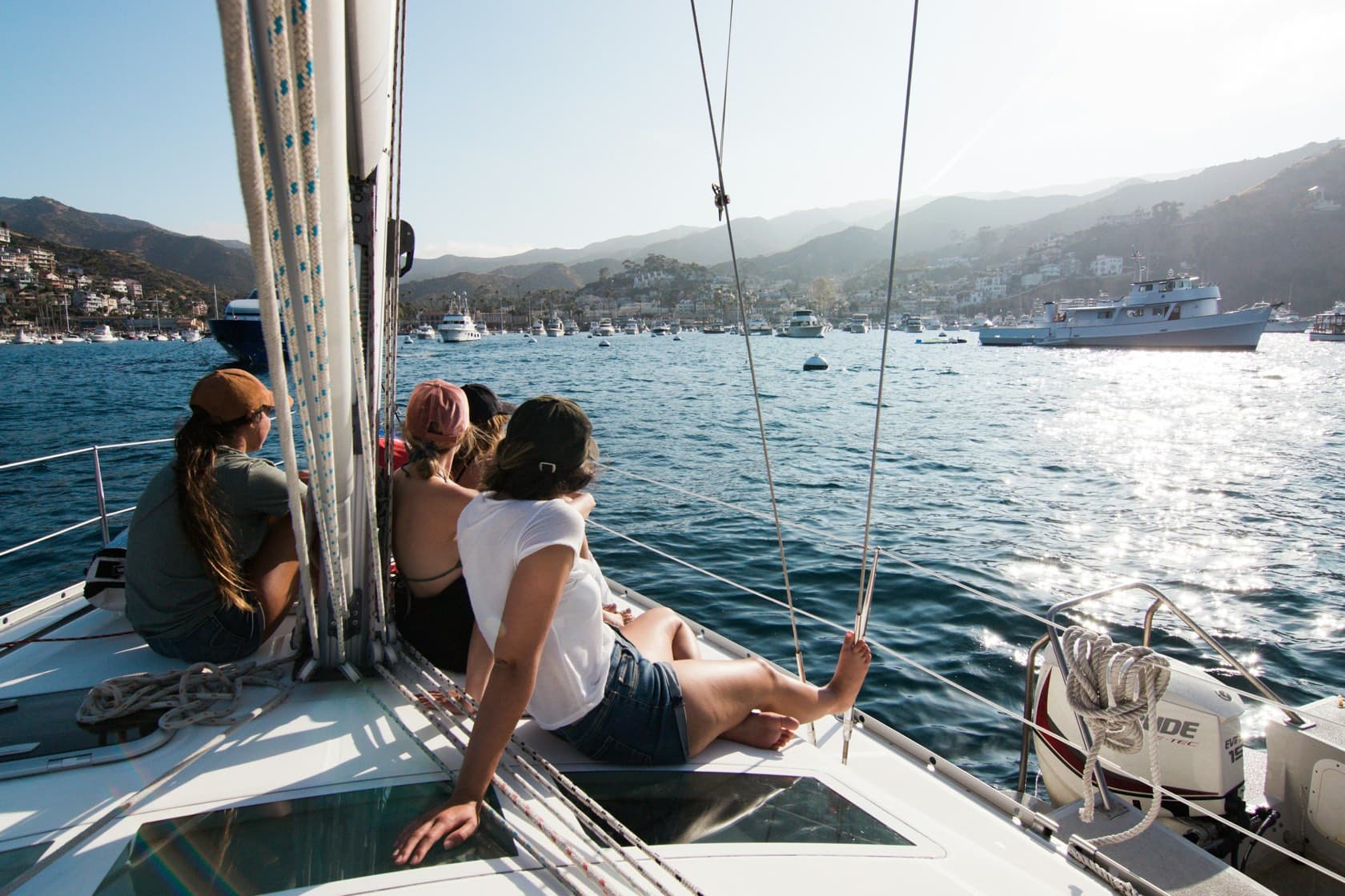 Personas sentadas en la proa de un velero frente a una bahía con cerros