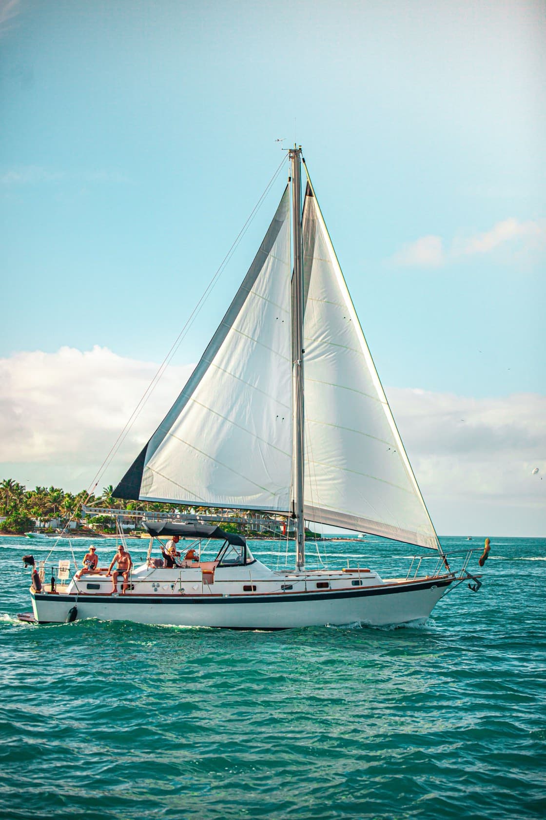 Velero blanco con las velas izadas y gente a bordo en agua turquesa